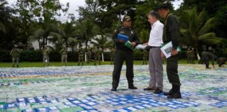 Juan Manuel Santos escucha a un miembro de la policía antinarcóticos encima de los paquetes de cocaína decomisados