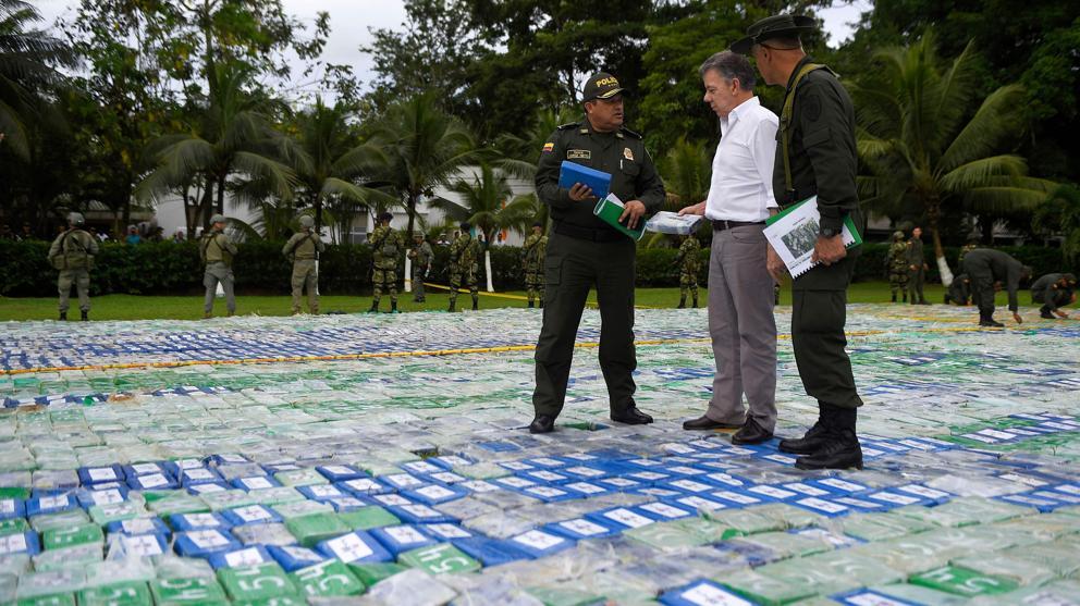 Juan Manuel Santos escucha a un miembro de la policía antinarcóticos encima de los paquetes de cocaína decomisados