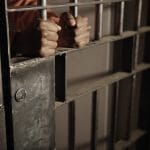Criminal in jail holding the bars of his prison cell