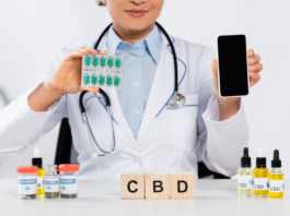 cropped view of african american doctor holding blister pack with capsules and smartphone with blank screen near cbd cubes and bottles