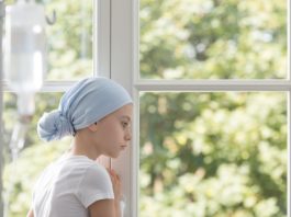 Sad sick child with cancer wearing blue headscarf during treatme