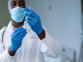 African american male doctor wearing face mask and gloves preparing covid vaccination