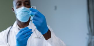 African american male doctor wearing face mask and gloves preparing covid vaccination