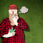cardboard man in plaid shirt holding cannabis and smoking on green grass background, marijuana legalization concept