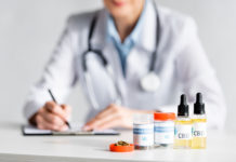 selective focus of dried marijuana, bottles with cbd and medical cannabis lettering near doctor writing prescription