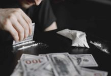 Young addicted man taking cocaine with dollar