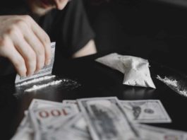 Young addicted man taking cocaine with dollar