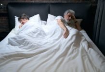 Old couple sleeping in hotel, man looking at camera