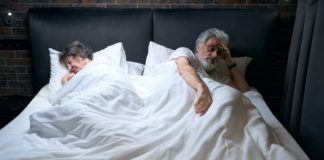 Old couple sleeping in hotel, man looking at camera