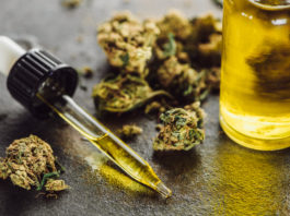close up view of medical marijuana buds, bottle and dropper with hemp oil on stone surface