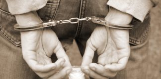 Arrested drug dealer in police handcuffs with small heroin drug