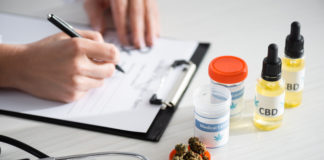 cropped view of doctor writing prescription near dried weed, bottles with cbd and medical cannabis