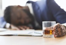 Drunk employee with glass of whiskey sleeping at working place