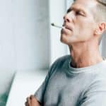 handsome man smoking blunt with medical cannabis in apartment