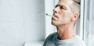 handsome man smoking blunt with medical cannabis in apartment