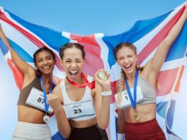 Cheerful diverse group of female olympic athletes holding winners medals and British flag. Happy an