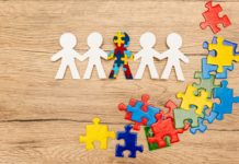 Top view of special kid with autism among another and pieces of bright colorful puzzle on wooden
