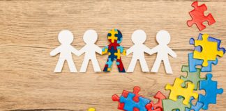 Top view of special kid with autism among another and pieces of bright colorful puzzle on wooden
