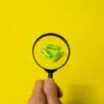 Crop person holding magnifier above pills