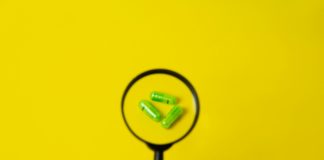 Crop person holding magnifier above pills