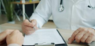 Medic in uniform is ticking symptoms in patient's medical records during appointment in clinic talking to patient sick woman. People and healthcare concept.
