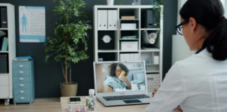 Young woman in doctor's uniform is talking to sick African American girl online using laptop in clinic giving medical advice. People and healthcare concept.