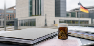 Documentaci&oacute;n sanitaria y un frasco neutro de cannabis medicinal ante un edificio institucional alem&aacute;n