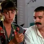 Una mujer sostiene un cigarrillo liado mientras un hombre con bigote observa su mano.