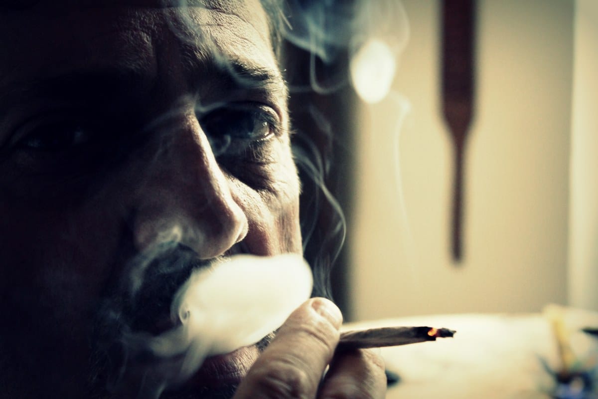 Primer plano de un hombre fumando un cigarrillo artesanal mientras exhala una nube de humo