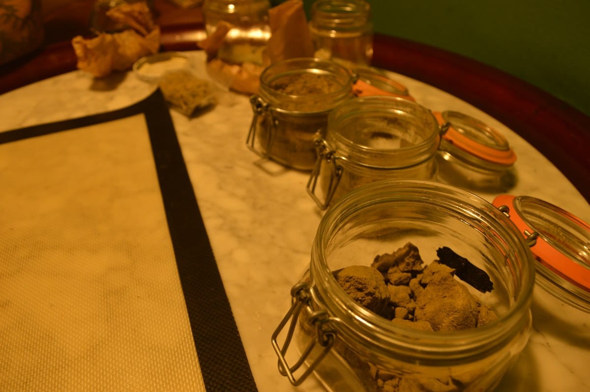 Tarros de vidrio con fragmentos marrones sobre una mesa junto a una l&aacute;mina de silicona