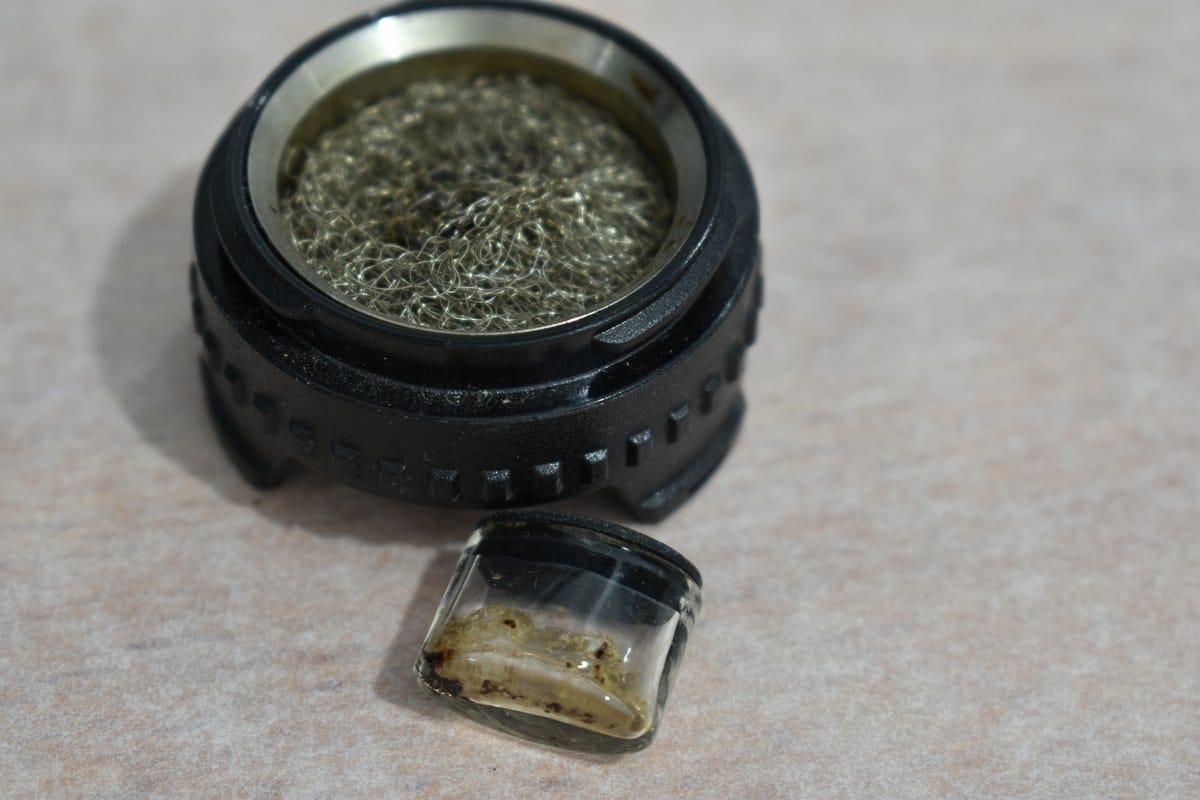 Cazoleta circular con malla metálica y pequeño recipiente de vidrio con restos de extracto