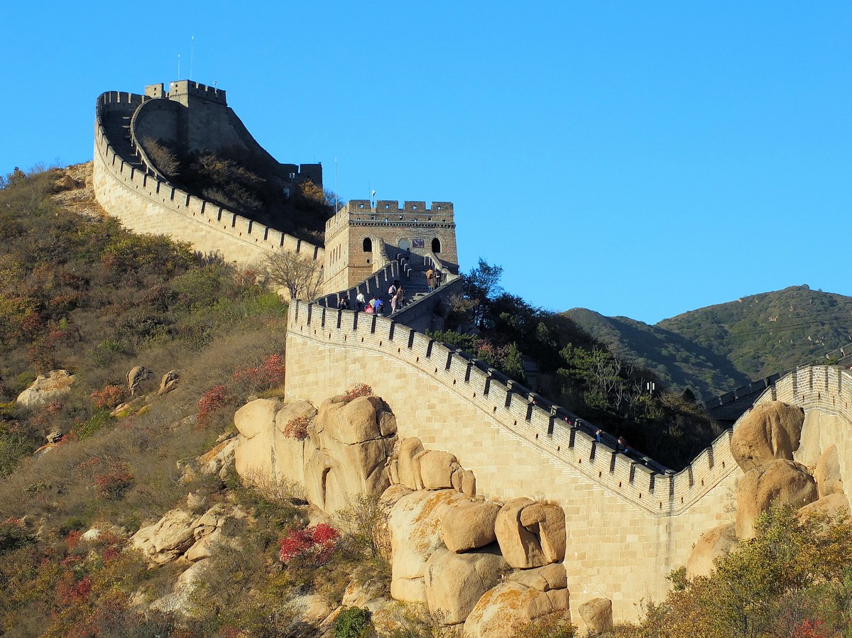 Muralla fortificada con torres que recorre una ladera rocosa y montañosa