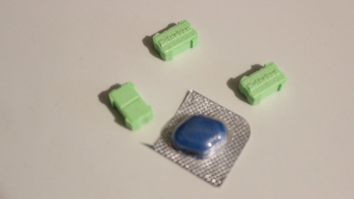 Comprimido azul en un blíster junto a tres pastillas verdes rectangulares