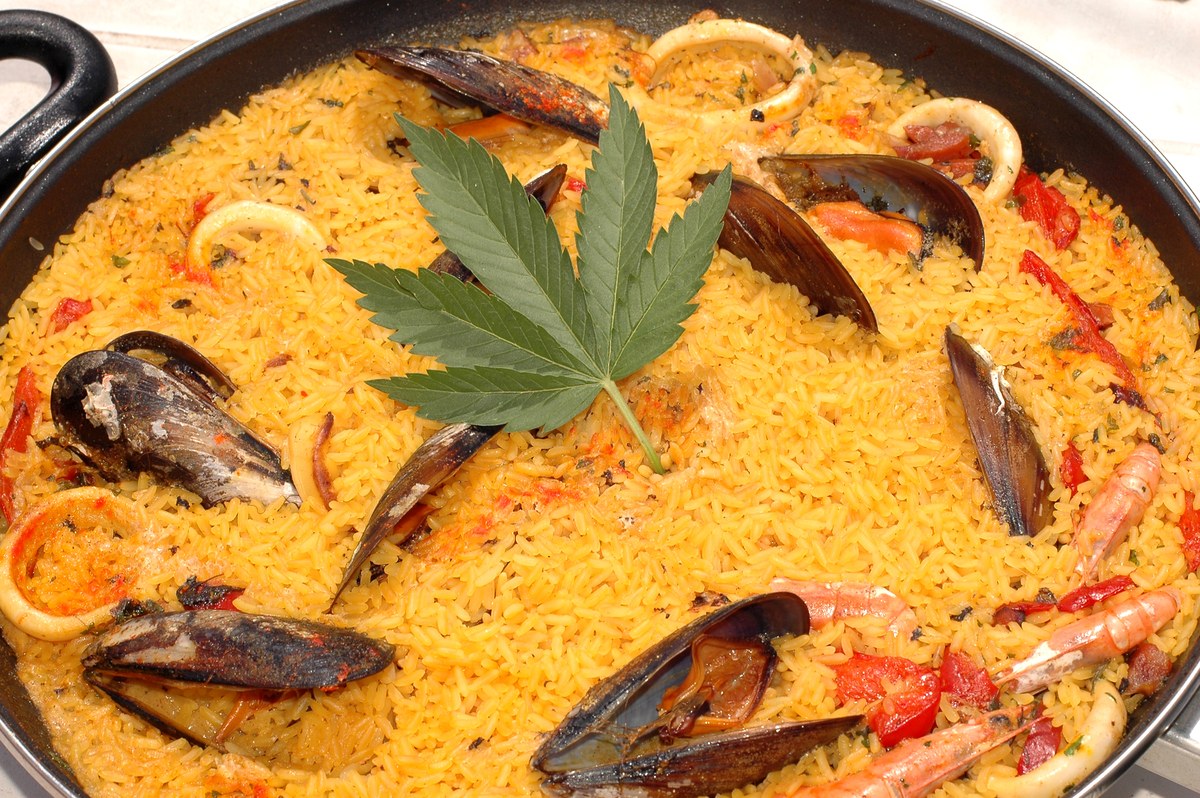Paella de marisco con mejillones, calamares, langostinos y una hoja de cannabis en el centro.
