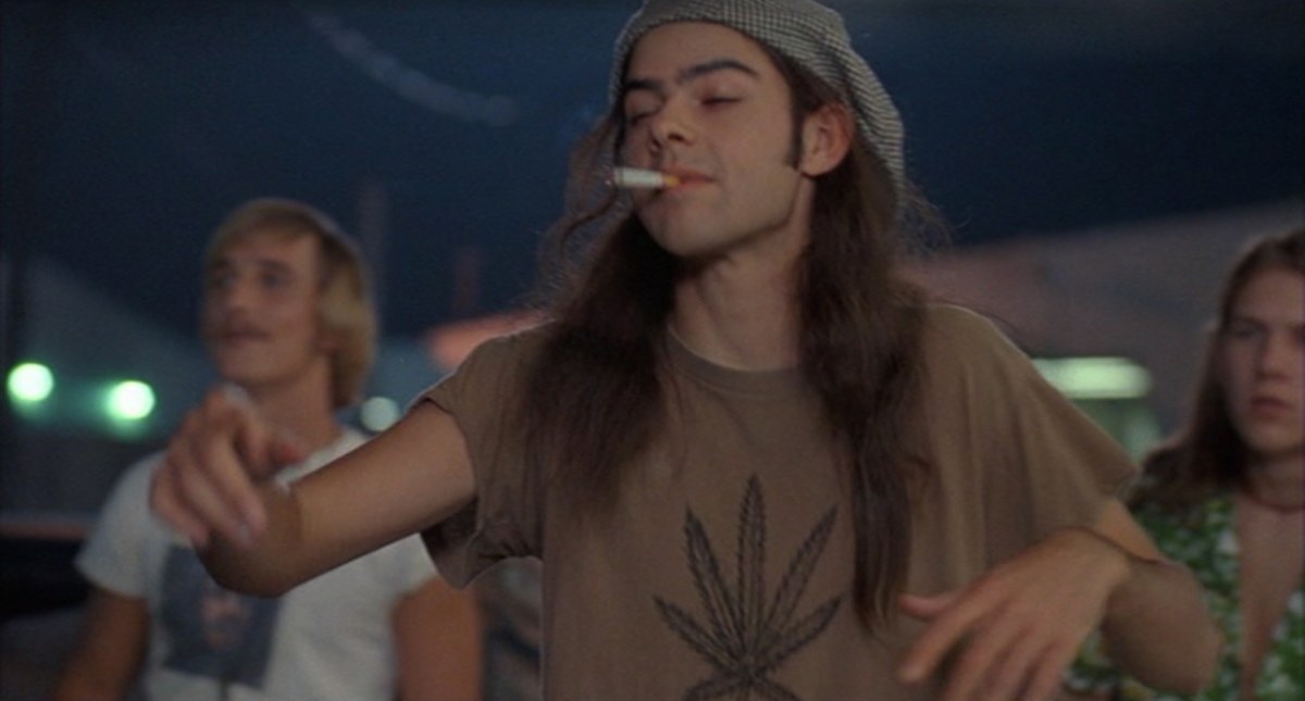 Joven con gorro fuma mientras baila con una hoja de cannabis estampada en la camiseta.