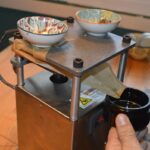 Prensa de extracci&oacute;n con papel plegado que dirige un l&iacute;quido oscuro hacia un frasco sostenido a mano.