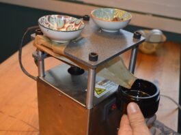 Rosin de hachís y líquido: variables y proceso Prensa de extracción con papel plegado que dirige un líquido oscuro hacia un frasco sostenido a mano.