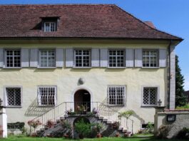 El cannabis en Heliópolis de Ernst Jünger Fachada de una casa histórica con tejado de tejas, ventanas enrejadas y escalinata adornada con flores.