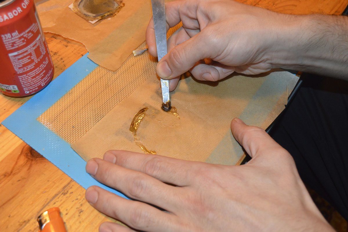 Manos recogen con una esp&aacute;tula un concentrado &aacute;mbar sobre papel de horno y una l&aacute;mina de silicona.