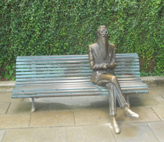 Valle-Inclán y sus primeras alusiones al cannabis Escultura de bronce de un hombre barbado con gafas, sentado con las piernas cruzadas en un banco