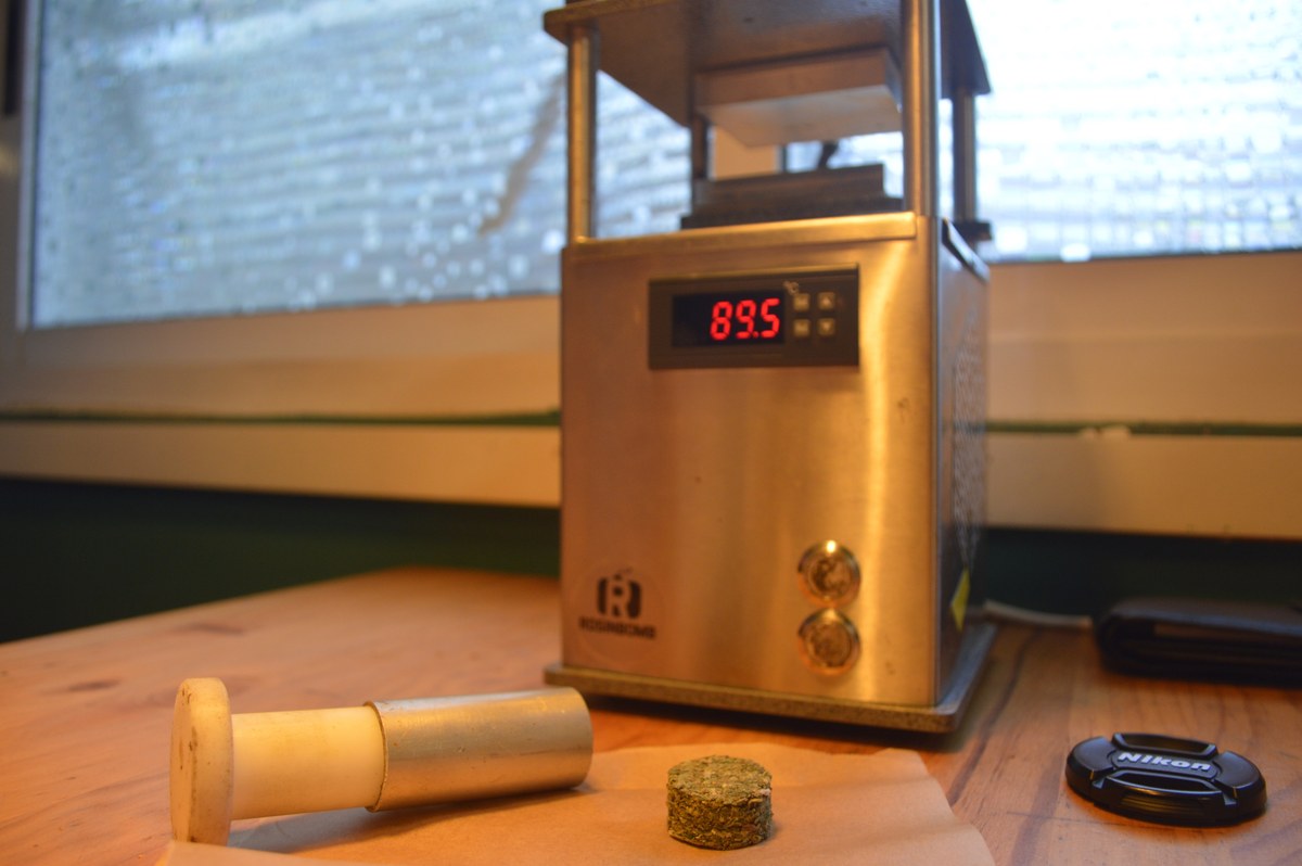 Prensa t&eacute;rmica con pantalla a 89,5 grados, molde cil&iacute;ndrico y pastilla de material vegetal sobre una mesa.