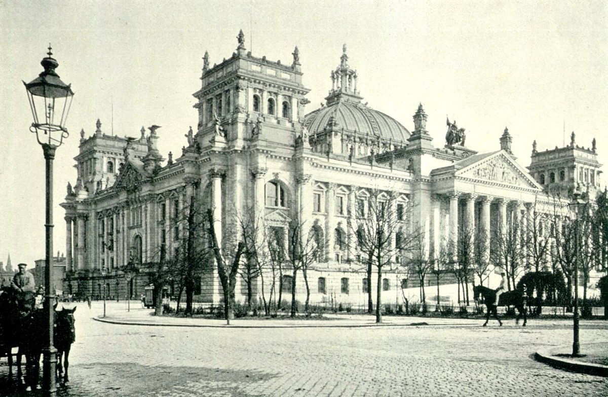 Vista hist&oacute;rica en blanco y negro de un edificio monumental con c&uacute;pula, columnas y carruajes en la calle.