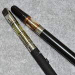 Dos dispositivos de vapeo con depósitos transparentes sobre una superficie gris
