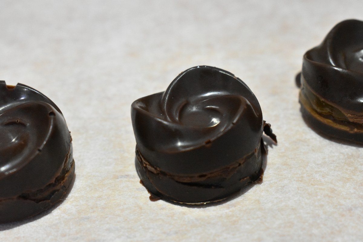 Tres bombones caseros de chocolate negro con forma circular sobre una superficie clara.