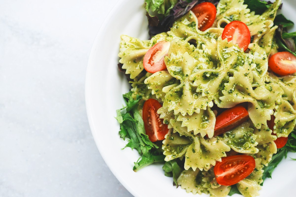 Ensalada de pasta con pesto, tomates cherry y hojas verdes sobre un plato blanco