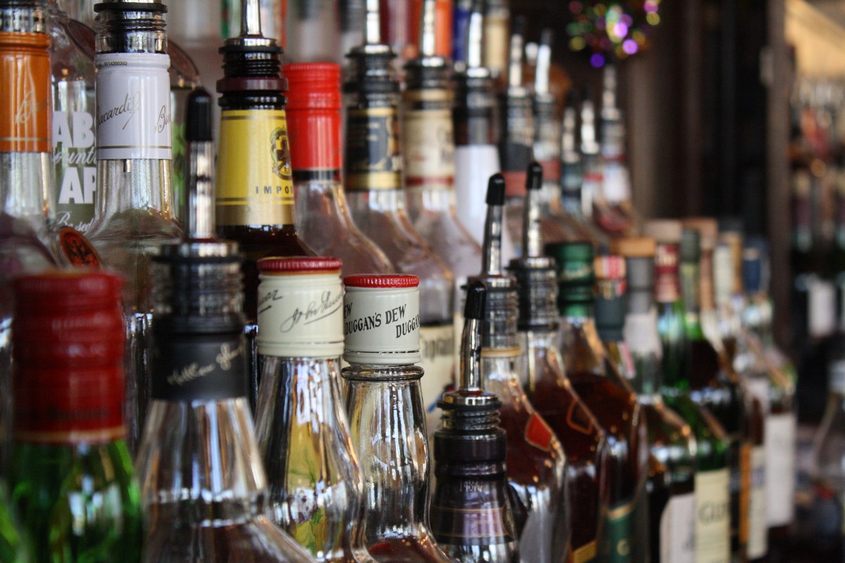 Filas de botellas de bebidas alcoh&oacute;licas con dosificadores sobre la barra de un local