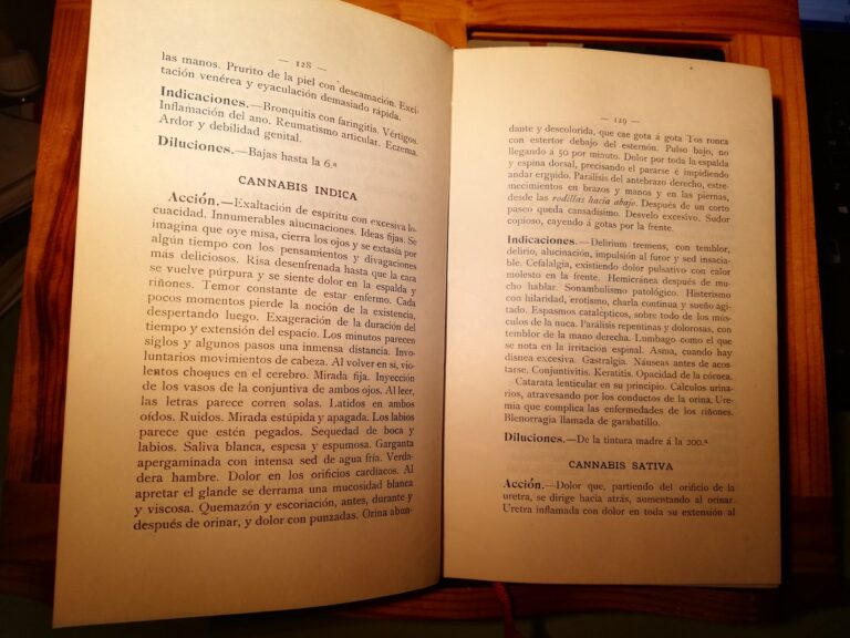 Libro abierto con descripciones en español de Cannabis indica y Cannabis sativa sobre una mesa de madera