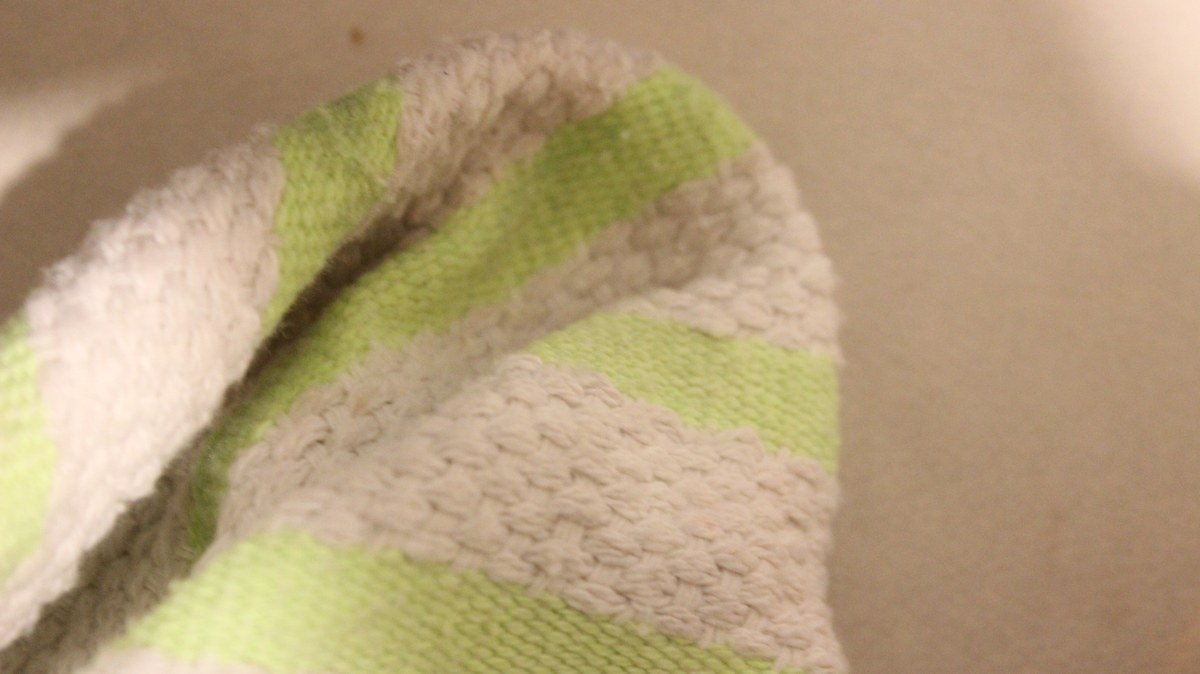 Primer plano de una toalla blanca con franjas verdes sobre una superficie beige
