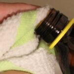 Mano sujetando con una toalla el cuello abierto de un frasco de vidrio ámbar