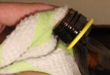 Historia del éter: anestesia y uso recreativo Mano sujetando con una toalla el cuello abierto de un frasco de vidrio ámbar